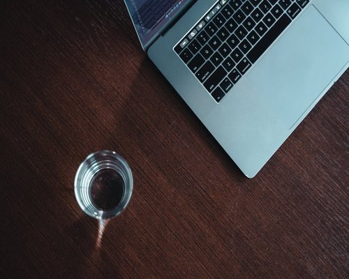 A clean glass of fresh drinking water resting on a minimalist wooden workspace desk