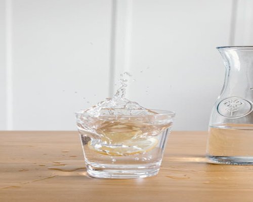 A clear glass pitcher with pure fresh water and a subtle slice of lemon inside